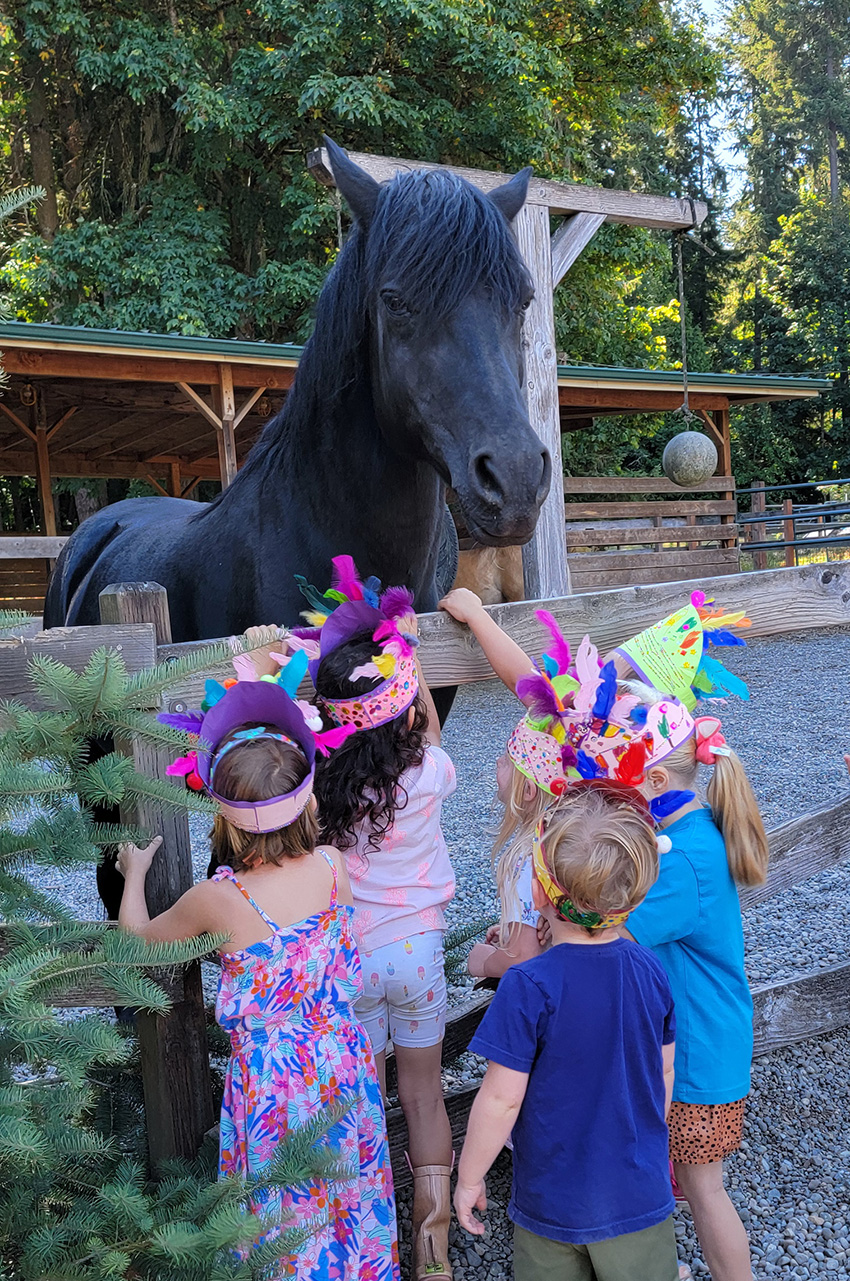 View larger image of Village Learning kids wearing headdresses while petting horse from outside the fence Kids wearing headdresses while petting horse from outside the fence